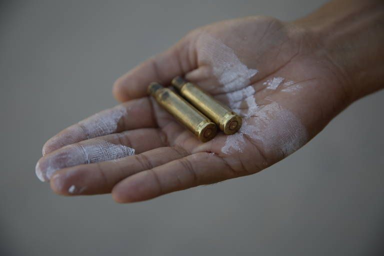 Na foto, uma mão segura duas balas de arma de fogo