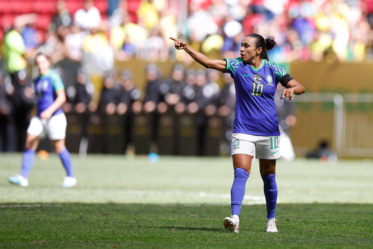 Marta, em campo, dá instruções a outras jogadoras com o braço direito estendido. Ela veste o uniforme azul da seleção e está com o cabelo preso em um coque