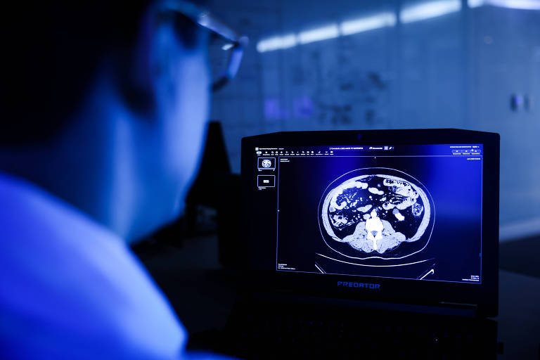 Médico olha tela de um monitor. Imagem é azulada.