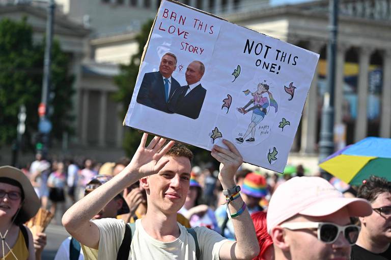 Durante Parada do Orgulho LGBT+ em Budapeste, participante segura cartaz que diz 'proíba essa história de amor', ao lado de imagem do premiê húngaro, Viktor Orbán, e do russo Vladimir Putin, 'não essa', ao lado de desenho de casal gay