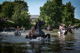 People with their horses in the River Eden during the Appleby Horse Fair in Appleby-in-Westmoreland, England, June 9, 2023. (Mary Turner/The New York Times)