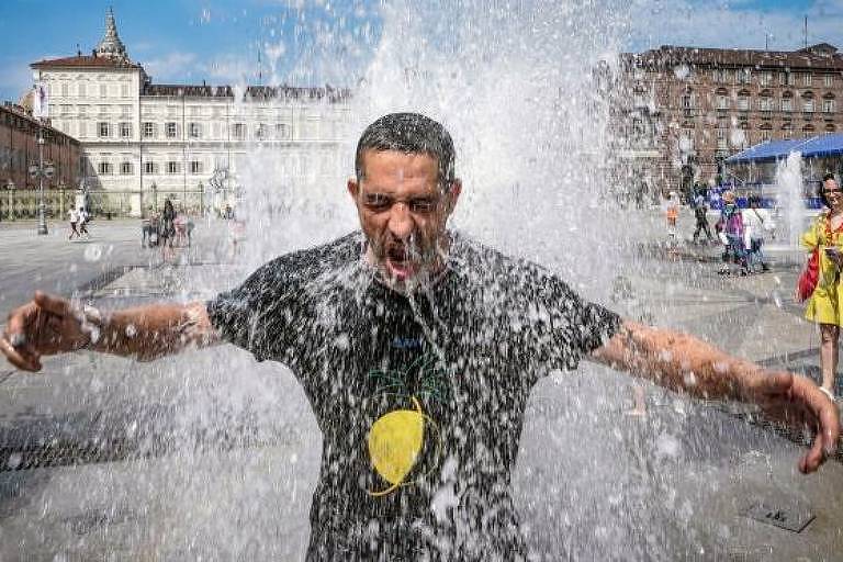 Um homem se refresca numa fonte, em Turim, na Itália