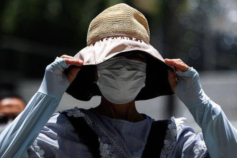 Mulher se protege do sol com um chapéu, na China
