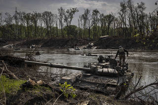 A Ukrainian soldier atop an abandoned Russian tank in the Siversky Donets River, in Bilohorivka, Ukraine, on May 24, 2022. (Ivor Prickett/The New York Times)