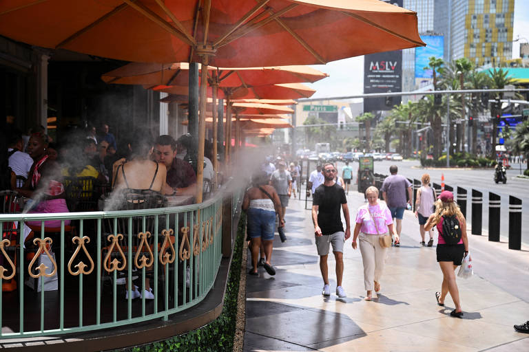 Imagem mostra pessoas andando na rua sob sol. Ao lado esquerdo, há uma varanda de um restaurante, onde umidificadores jogam uma nuvem de água para a calçada.
