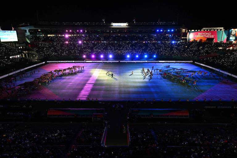 Campo iluminado nas cores rosa azul e branco durante performance artística