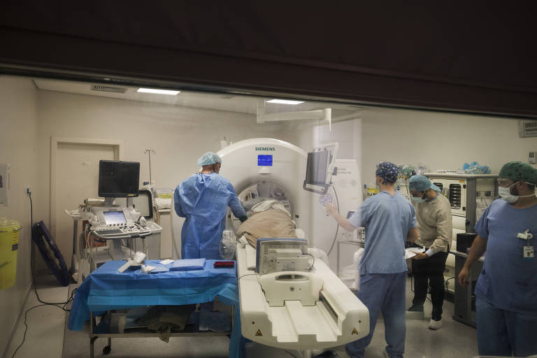 Imagem mostra quatro profissionais de saúde paramentados em torno de um equipamento de tomografia