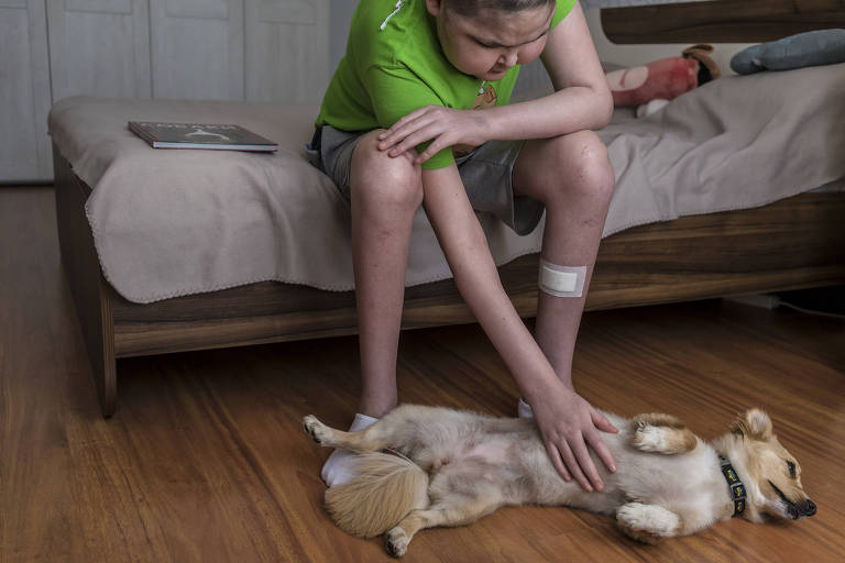 Sasha Batanov, que está sendo tratada de leucemia, brinca com Cassandra, cachorra de um especialista em habitação ambulatorial da instituição de caridade Tabletochki, em Kiev