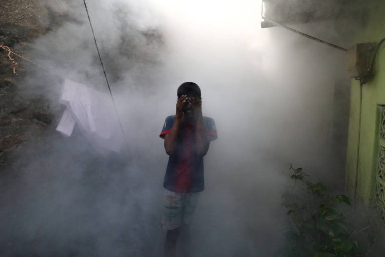 Garoto cobre o rosto no meio da fumaça de veneno pulverizada por trabalhadores do serviço de saúde do Sri Lanka, devido ao surto de dengue no país asiático