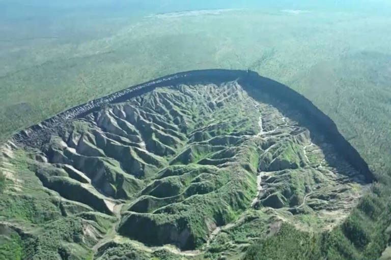 Vista aérea de paisagem com vegetação rasteira e enorme cratera onde o solo cedeu
