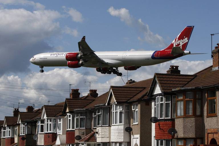 Aeronave da Virgin Atlantic chega ao aeroporto de Heathrow, em Londres; é possível ver casas baixas com tijolos aparentes e telhados marrons com antenas e janelas brancas