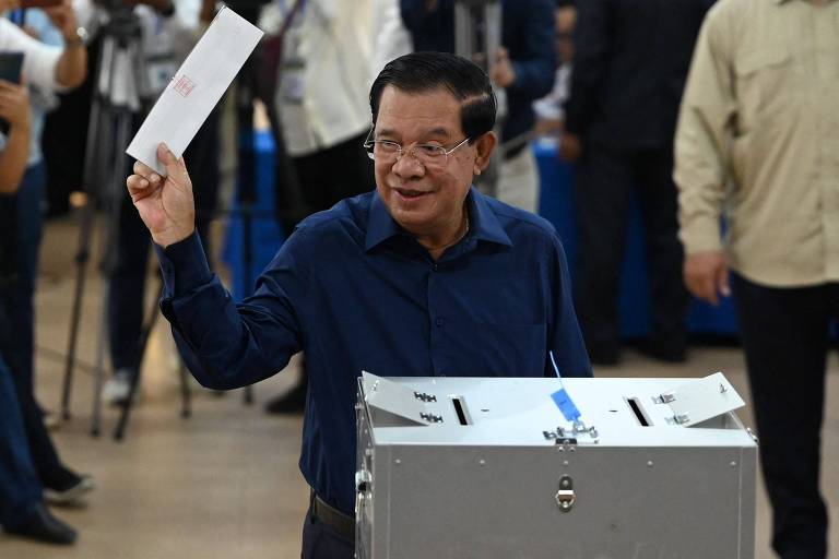 Homem idoso asiático de óculos e camisa azul segura envelope diante de urna