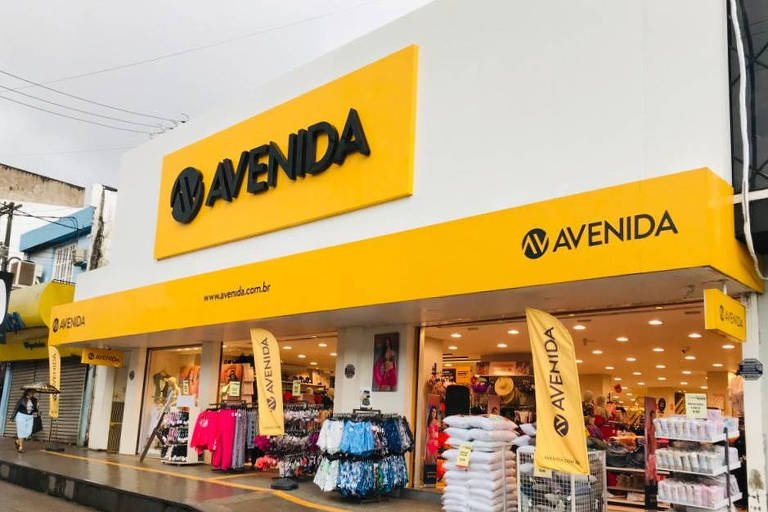 Imagem mostra entrada de uma loja do Grupo Avenida. Identidade visual da loja é amarela, com a palavra "Avenida" escrita na cor preta