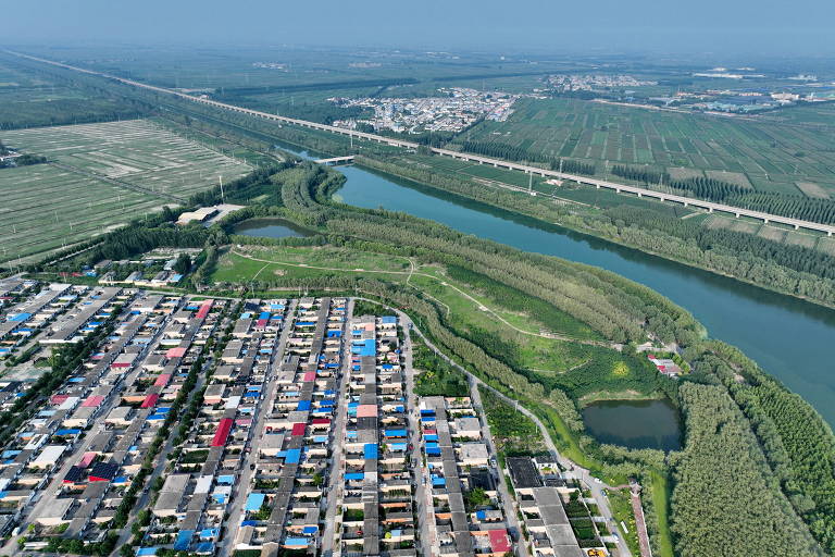 Imagem aérea mostra casas em vilarejo cercadas de vegetação. Um rio corta o cenário.