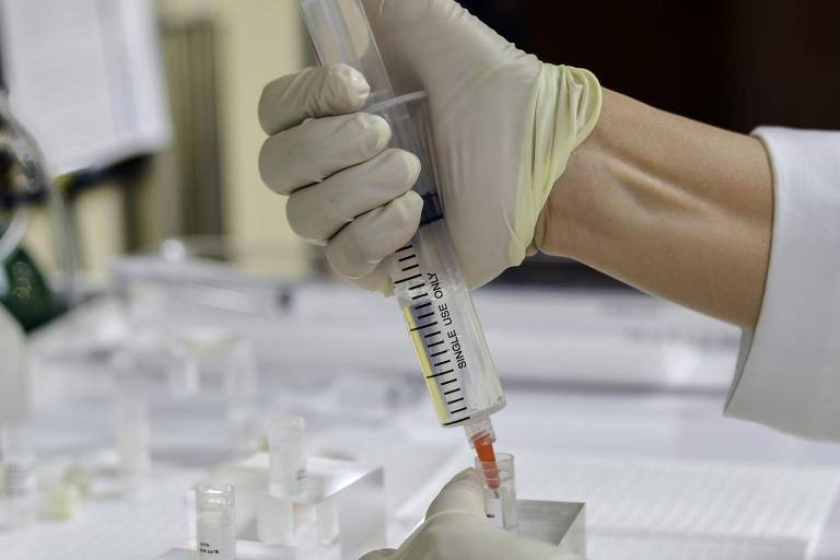 Mão de médico com luva colocando células-tronco em uma seringa em laboratório
