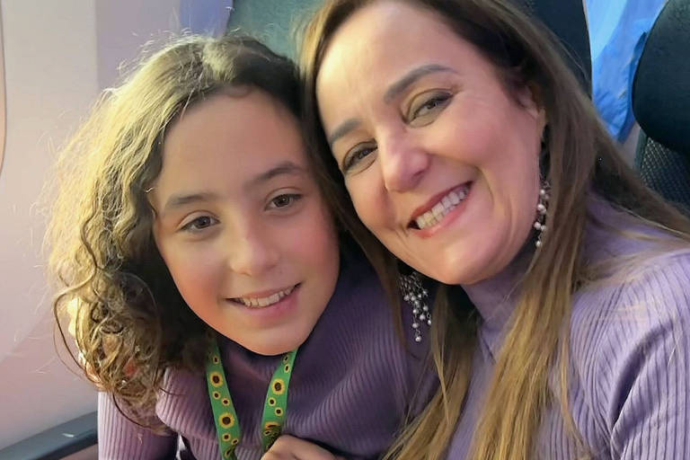 Mãe e filha sentadas em poltronas de avião; a garota usa um cordão verde estampado com girassóis