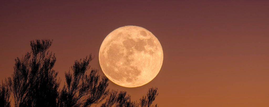 Lua cheia alarajada em um céu com tons de laranja e rosa 