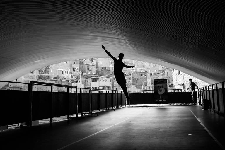 Foto em preto e branco mostra uma pessoa executando um salto artístico de ballet em um corredor; é possível ver apenas a silheta da pessoa registrada