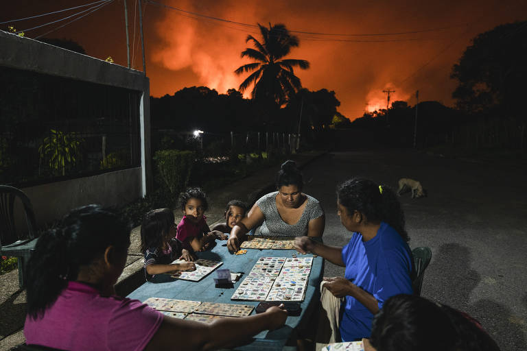 Vizinhos brincam com jogos de tabuleiro enquanto o céu é iluminado por explosões de poços de petróleo em Punta de Mata
