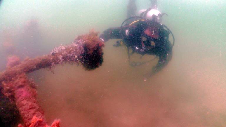 Mergulhador com cilindro de oxigênio e máscara segura em parte do que seria um navio afundado