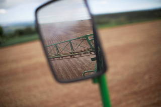 A side-view mirror of a tractor shows herbicide being sprayed in a field of soybeans, near Brasilia