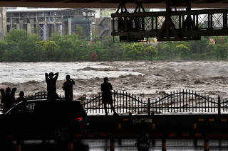 People look at the overflowing Yongding River following heavy rainfall in Beijing