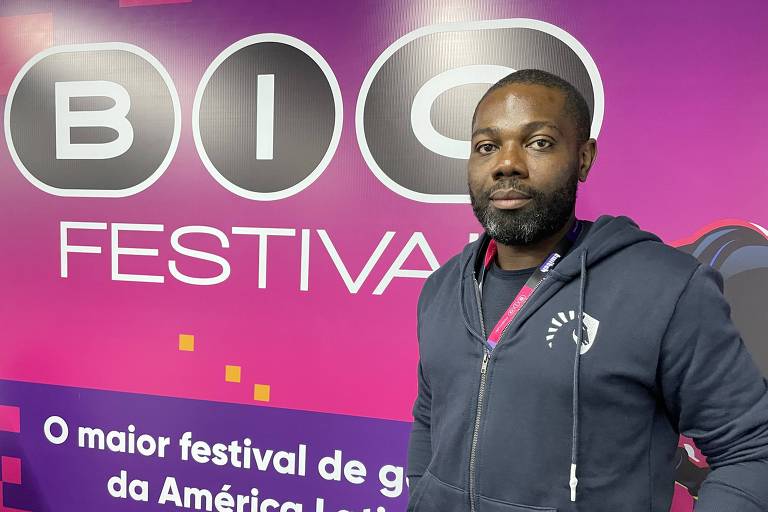 Homem negro vestindo uma blusa de moleton cinza escuro em frente a um painel roxo do BIG Festival