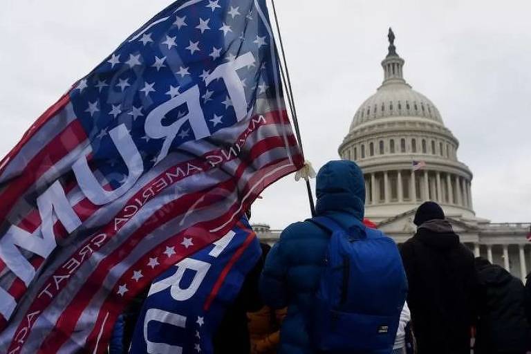 Homem em frente ao Capitólio, nos EUA, segura bandeira do país com nome do Trump