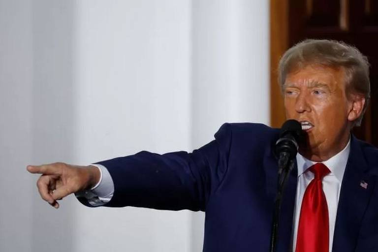 Donald Trump fala ao microfone e aponta com a mão direita para frente