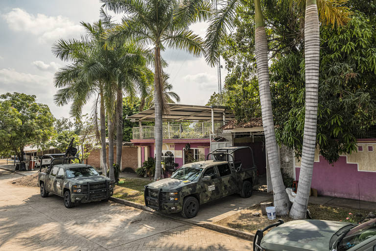 Carros militares em frente a casa que tem coqueiros em frente