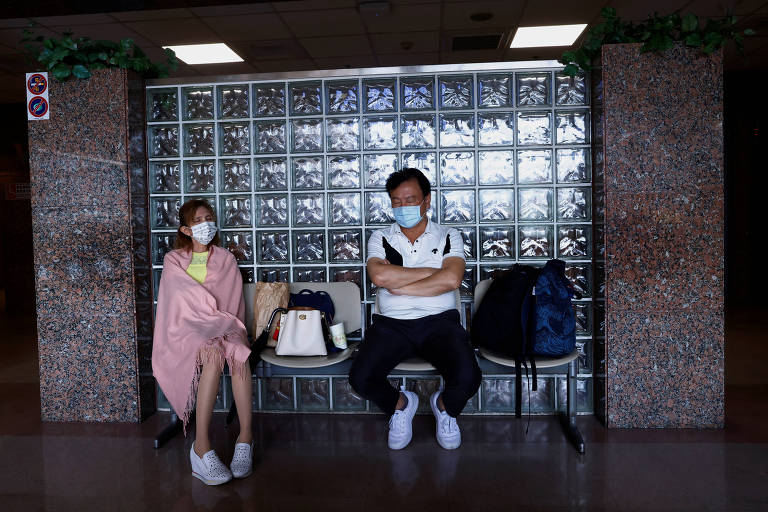 Casal vestindo máscaras sobre a boca aguarda filha em saguão de hospital