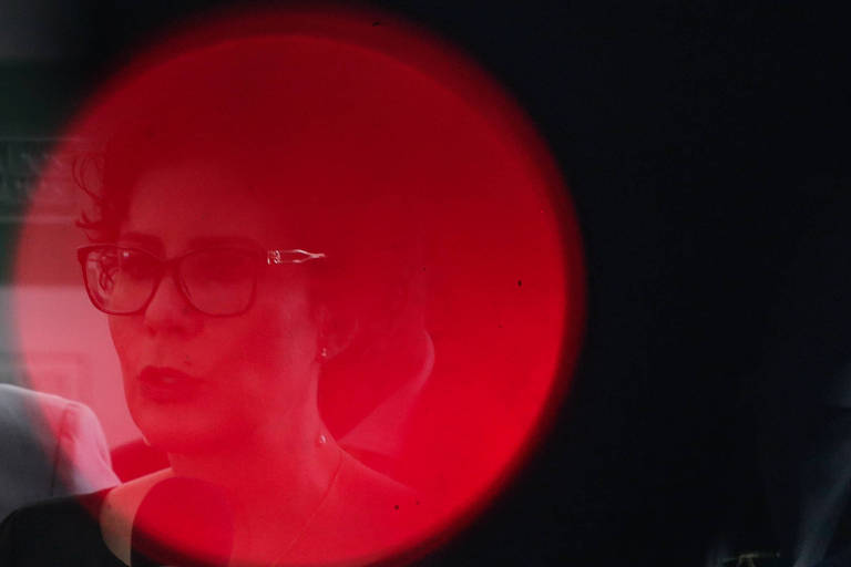 Rosto de Carla Zambelli, uma mulher branca, de cabelo curto e óculos de grau, em um círculo de luz vermelha.