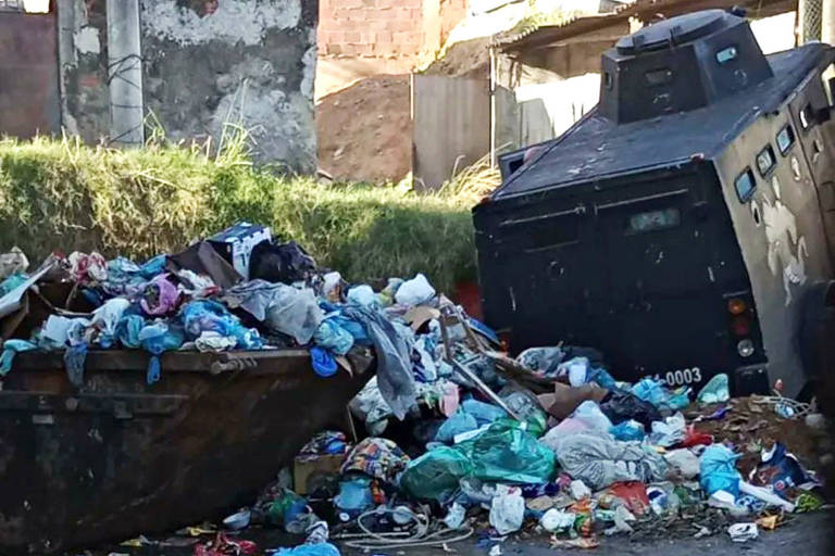Na imagem, veículo blindado da PM aparece tombado em cima de montanha de lixo na rua