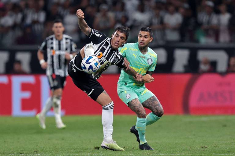 O jogador Saravia, do Atlético Mineiro, disputa a bola com Dudu, do Palmeiras, durante um jogo no estádio Mineirão. Um jogador do Atlético-MG, não identificado, aparece em segundo plano.