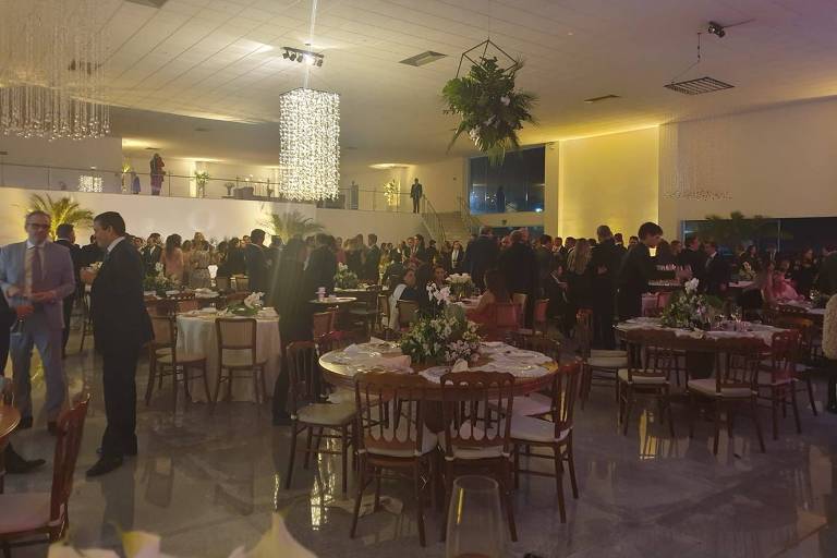 Um salão de festa em Brasília, com os presentes circulando pelo local.