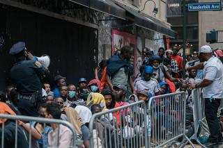 Migrants waiting to be processed queue outside of the Roosevelt Hotel in Manhattan, on Tuesday, Aug. 1, 2023. (Jeenah Moon/The New York Times)