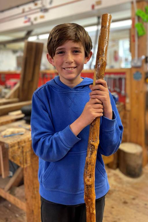 Menino de 10 anos que veste moletom azul segura pedaço de madeira e sorri para a foto