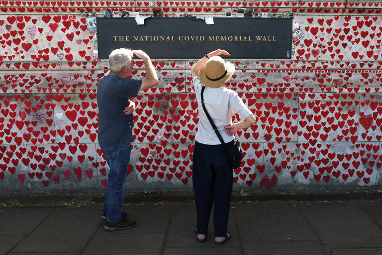 Um homem e uma mulher protegem os olhos do sol em frente ao memorial dedicado às vítimas de Covid