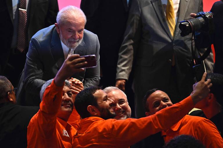Imagem mostra Lula e outras pessoas posando para selfie de celular.