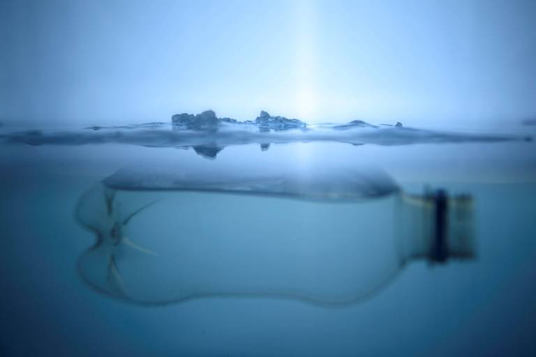 Garrafa é vista dentro da água do mar; há uma geleira ao fundo