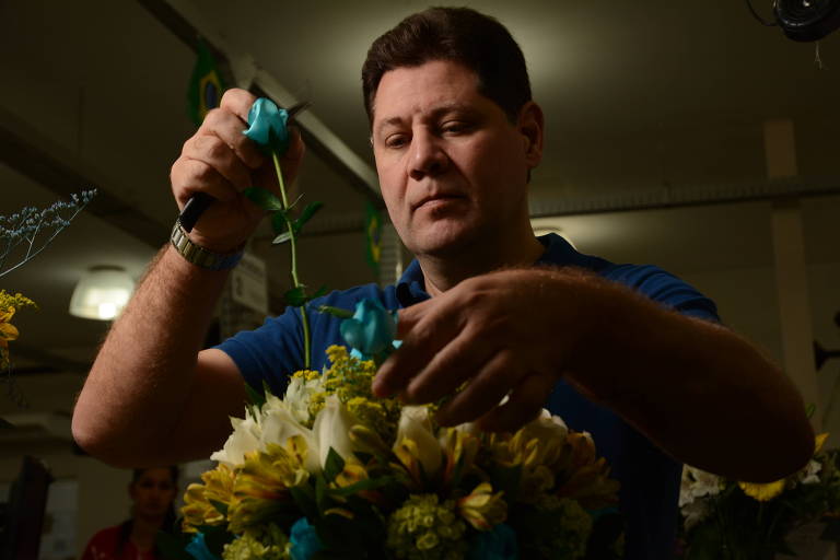 homem branco de camisa azul mexe em arranjo de flores