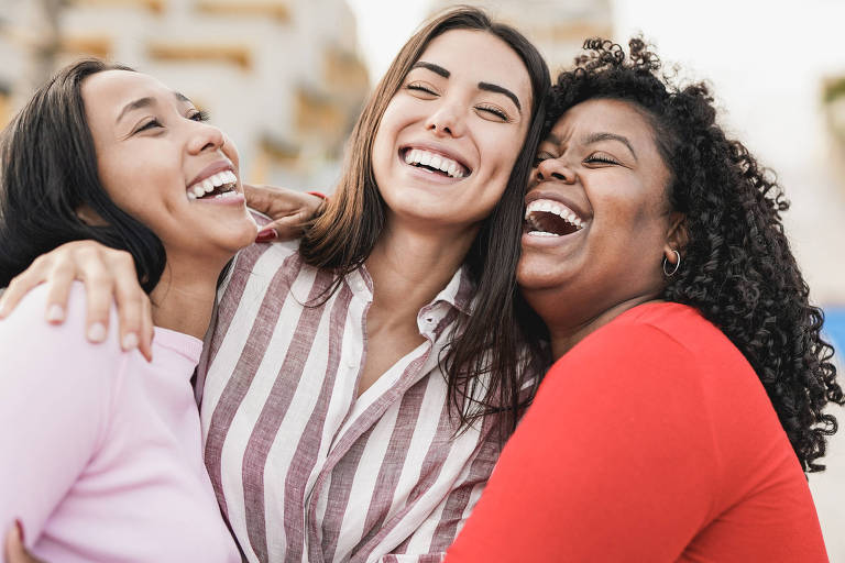 Duas mulheres latinas e uma mulher negra se abraçam sorrindo