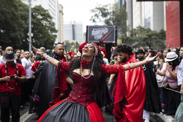 Mulher com vestido vermelho, de braços abertos, em meio a dezenas de pessoas na marcha, na avenida Paulista