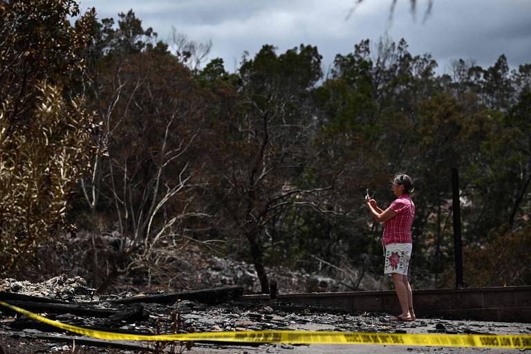 Mulher tira foto de local onde ficava sua casa, destruída pelas chamas em Maui, no Havaí