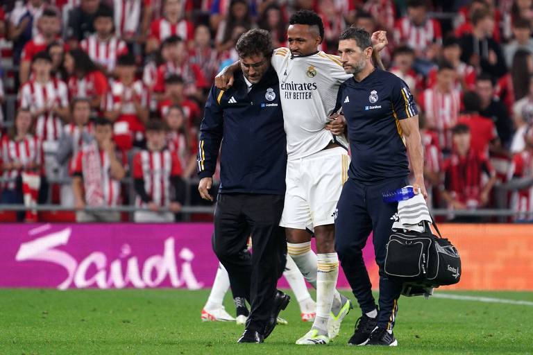 Amparado por funcionários do Real Madrid, o zagueiro Éder Militão deixa o campo depois de sofrer lesão contra o Athletic Bilbao no Campeonato Espanhol
