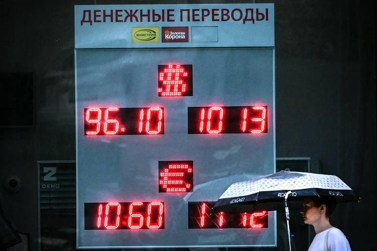 Moscovita passa em frente a casa de câmbio nesta terça (14), com taxa indicando 96,1 rublos por dólar