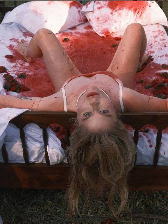Em foto colorida, mulher aparece deitada em uma cama toda manchada de sangue