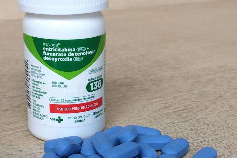 Foto mostra um frasco de medicamento sob uma mesa e, logo à sua frente, os próprios comprimidos; esses de cor azul escuro
