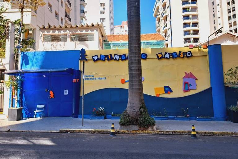 Muro pintado de azul e amarelo com o nome da escola