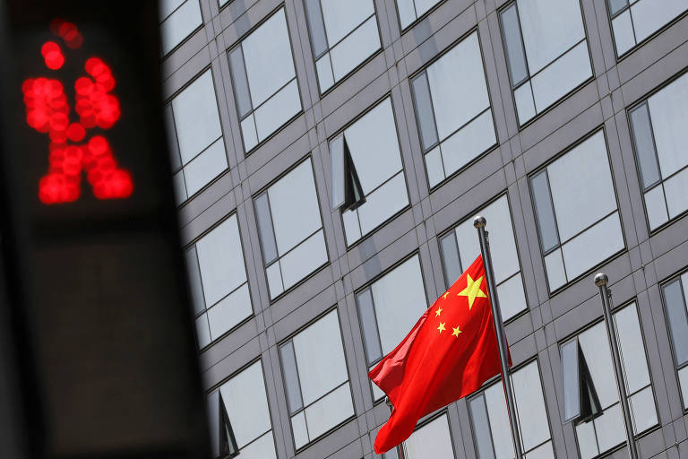 Imagem mostra bandeira chinesa hasteada em um mastro em frente a um prédio. Em primeiro plano, é possível ver um semáforo.